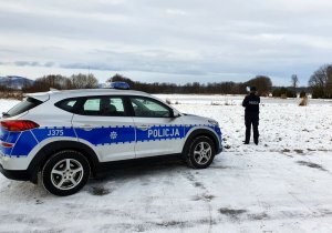 policjantka kontroluje zamarznięty staw, wokół zimowa sceneria i stojący radiowóz
