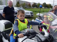 Chłopczyk siedzi na policyjnym motocyklu pod nadzorem policjanta.