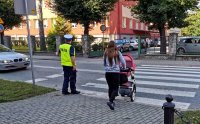 Kobieta z wózkiem przechodzi przez oznakowane przejście dla pieszych, które nadzorowane jest przez prudnickich policjantów ruchu drogowego.