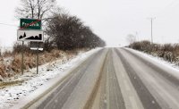 Na zdjęciu widoczne trudne warunki drogowe. Śnieg leżący na jezdni oraz w tle przyroda.