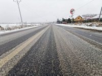 Na zdjęciu widoczne trudne warunki drogowe. Śnieg leżący na jezdni oraz w tle przyroda.