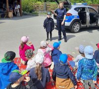 grupa dzieci siedząca na kocu słucha prelekcji policjantki