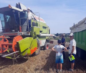 Policjanci rozmawiają z rolnikami na temat bezpieczeństwa podczas żniw. W tle traktor oraz kombajn.